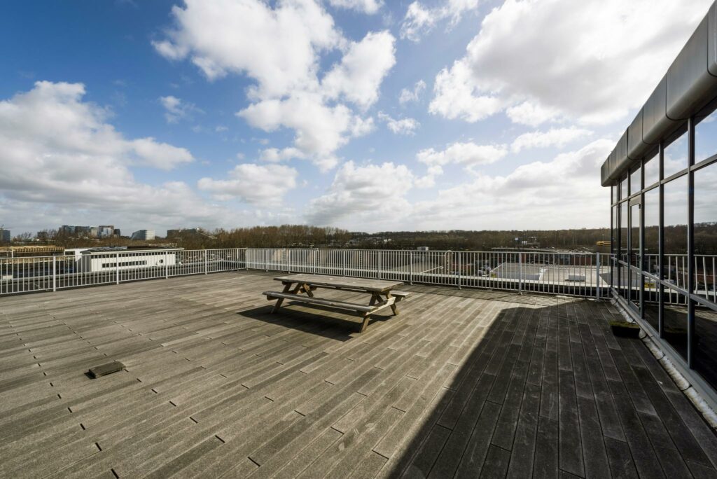 Ruim dakterras met picknicktafel en uitzicht op gebouwen aan de Anthony Fokkerweg onder een deels bewolkte lucht.